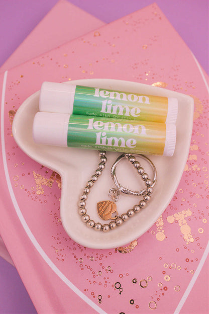 Two Lemon Lime flavoured lip balms displayed in a jewelry dish with a ring and bracelet, sitting on top of books.