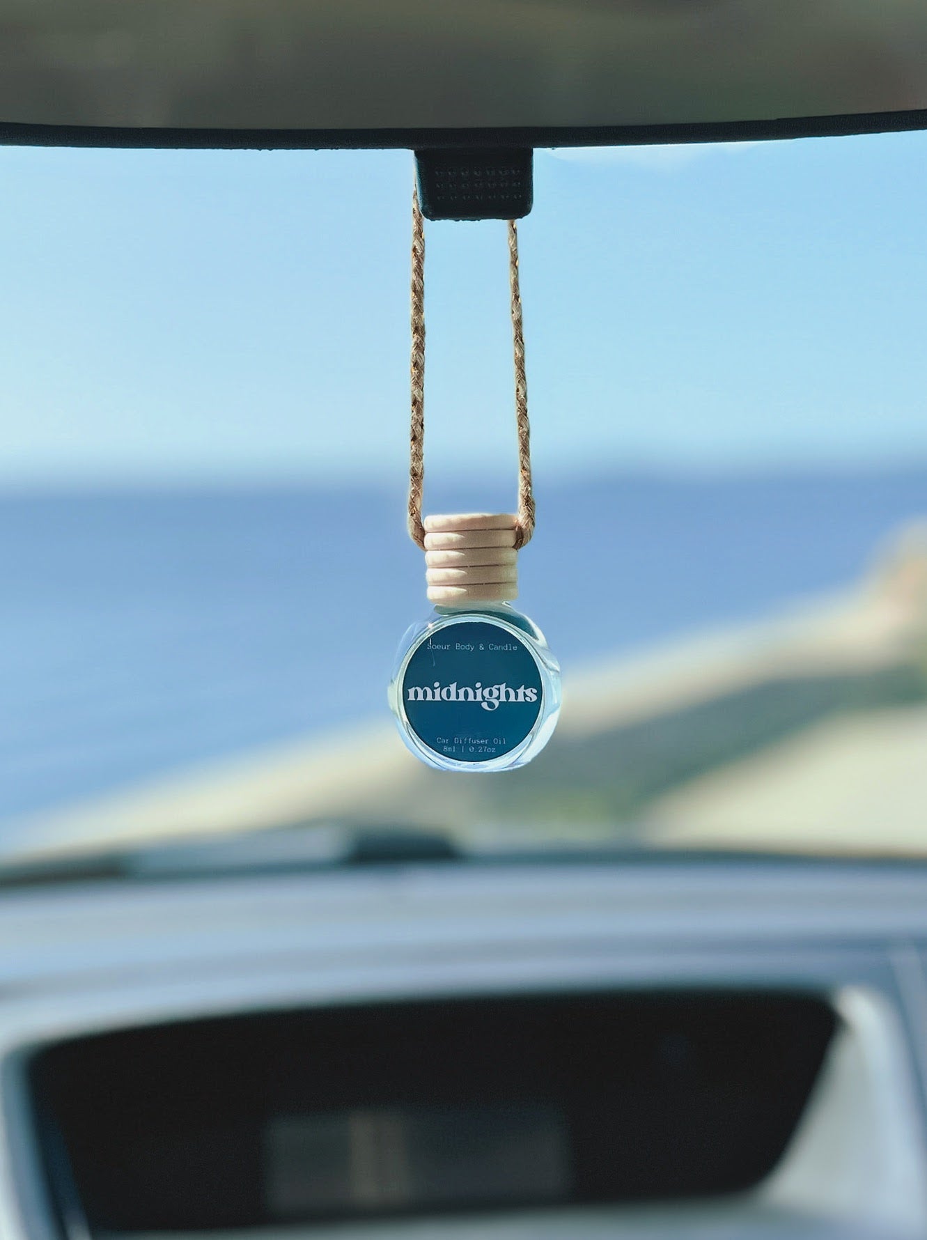 Midnights Diffuser Oil hanging from a rearview mirror, offering a balanced, long-lasting fragrance of pear, pepper, jasmine, coffee, and vanilla. Perfect for cars, closets, lockers, and more.