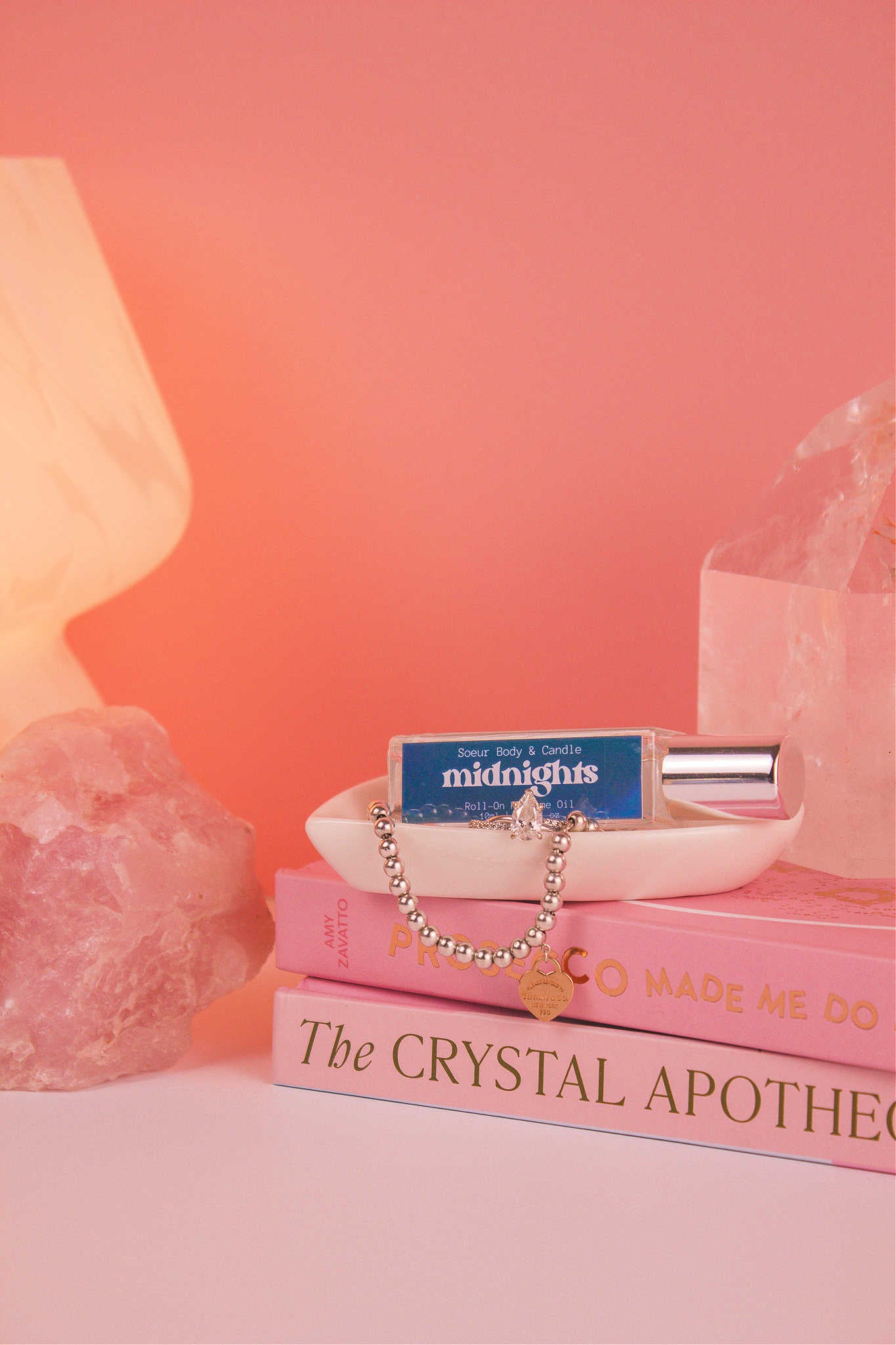 Midnights roll-on perfume elegantly displayed in a jewelry dish with coordinating jewelry, on top of books. Featuring notes of pear, pepper, jasmine, coffee, and vanilla.