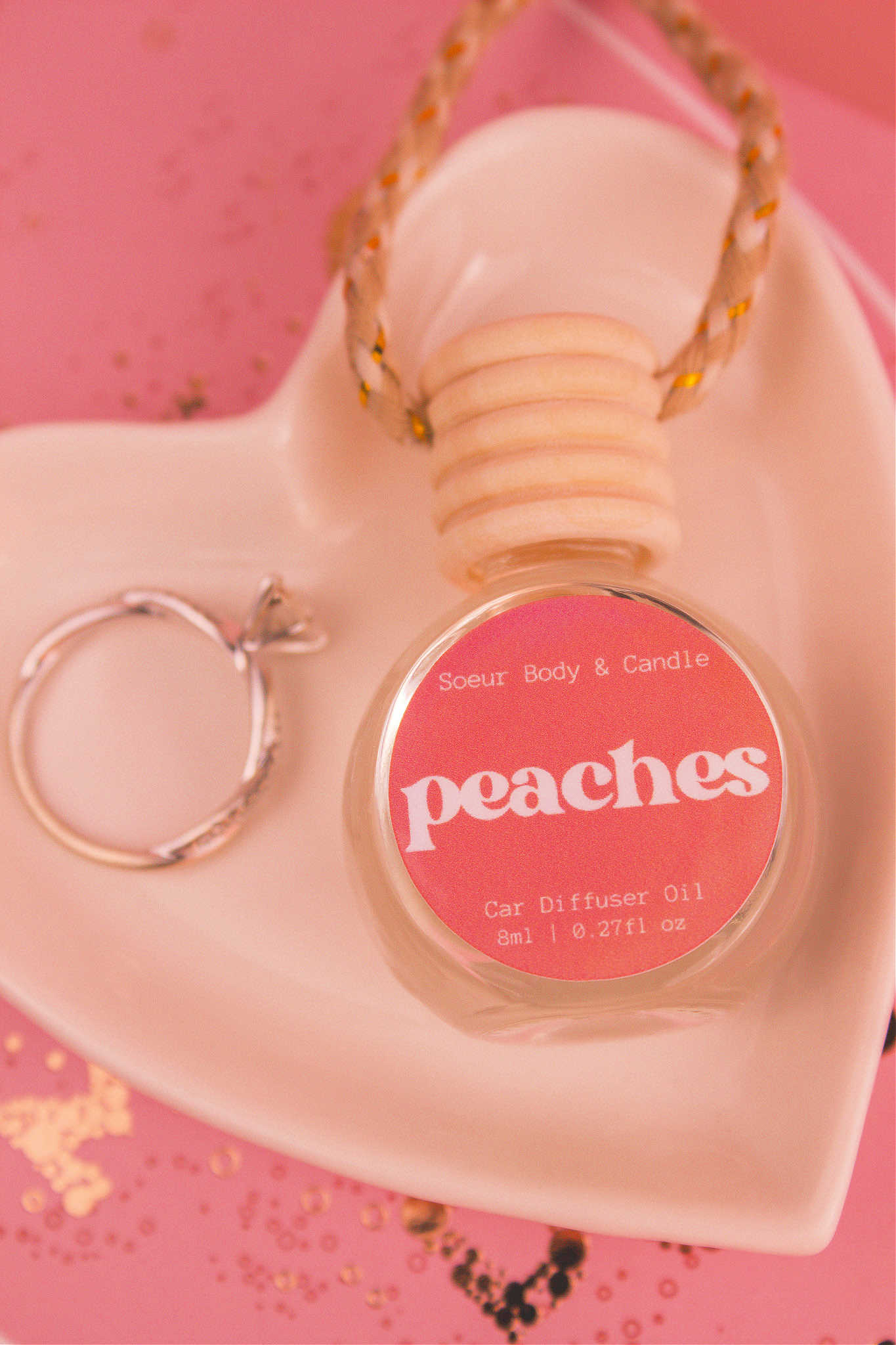 Close-up of Peaches car diffuser in a jewelry dish with a ring beside it, featuring notes of orange, persimmon, jasmine, peach, and musk.