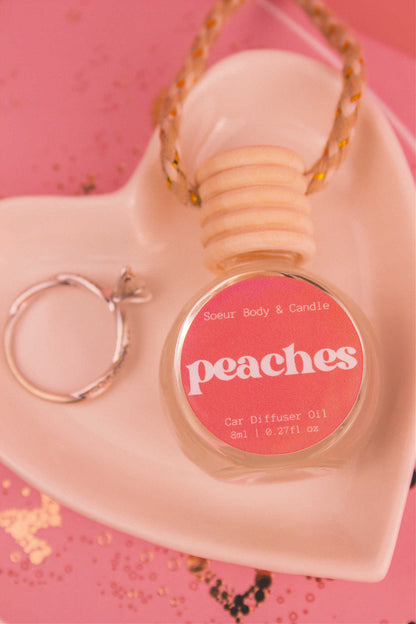 Close-up of Peaches car diffuser in a jewelry dish with a ring beside it, featuring notes of orange, persimmon, jasmine, peach, and musk.