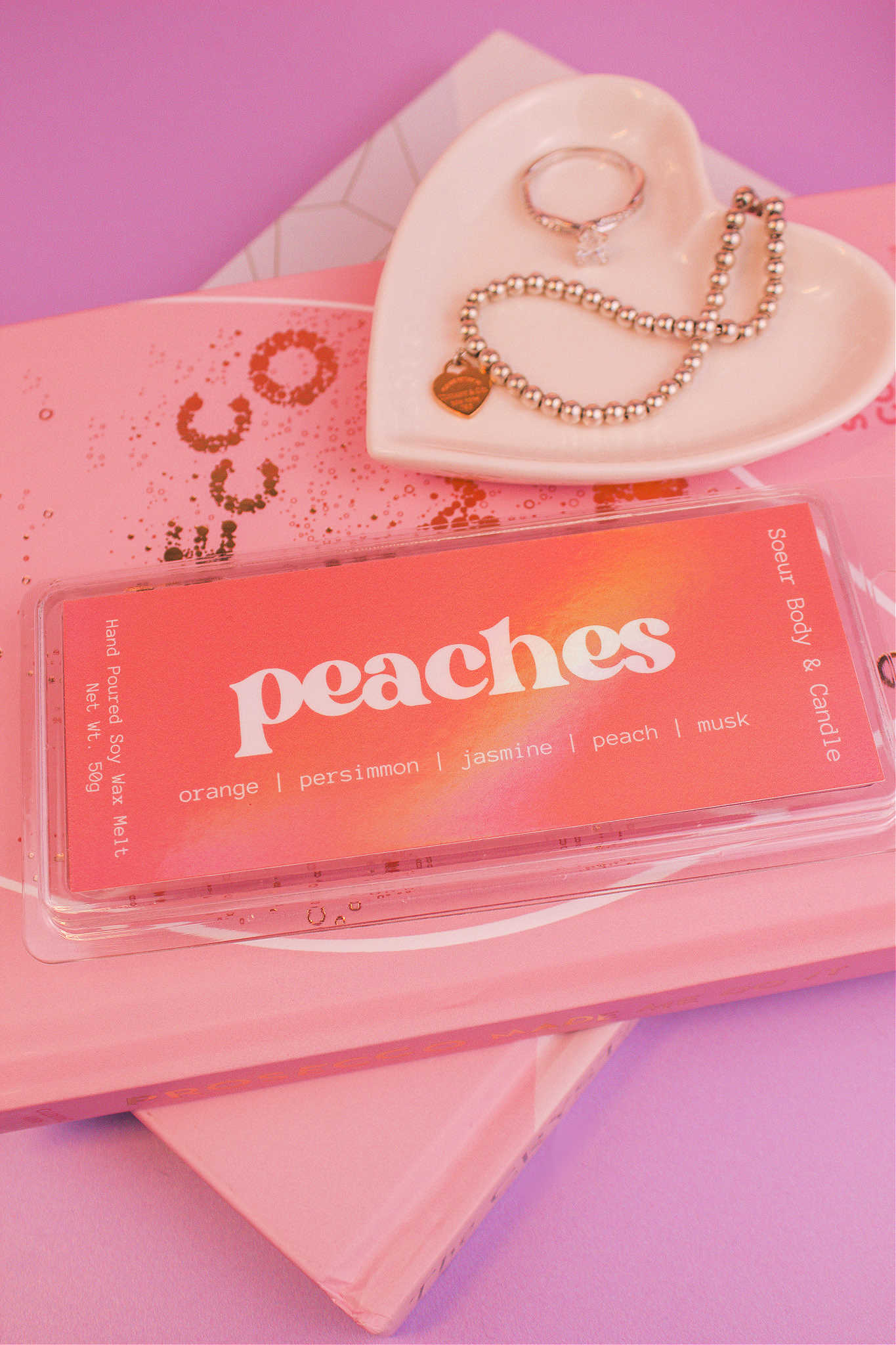 Close-up of Peaches wax melt displayed on books with a jewelry dish and jewelry visible in the background, showcasing its orange, persimmon, jasmine, peach, and musk notes.