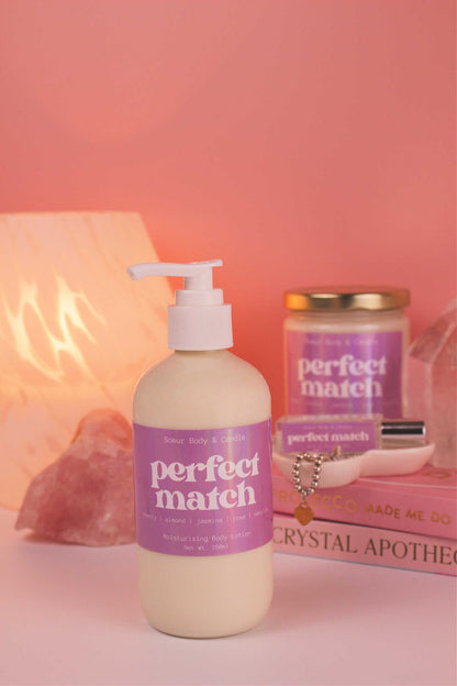 Perfect Match body lotion with matching candle and roll-on perfume, books, a lamp, and crystals in the background; highlighting cherry, almond, jasmine, rose, and vanilla notes.