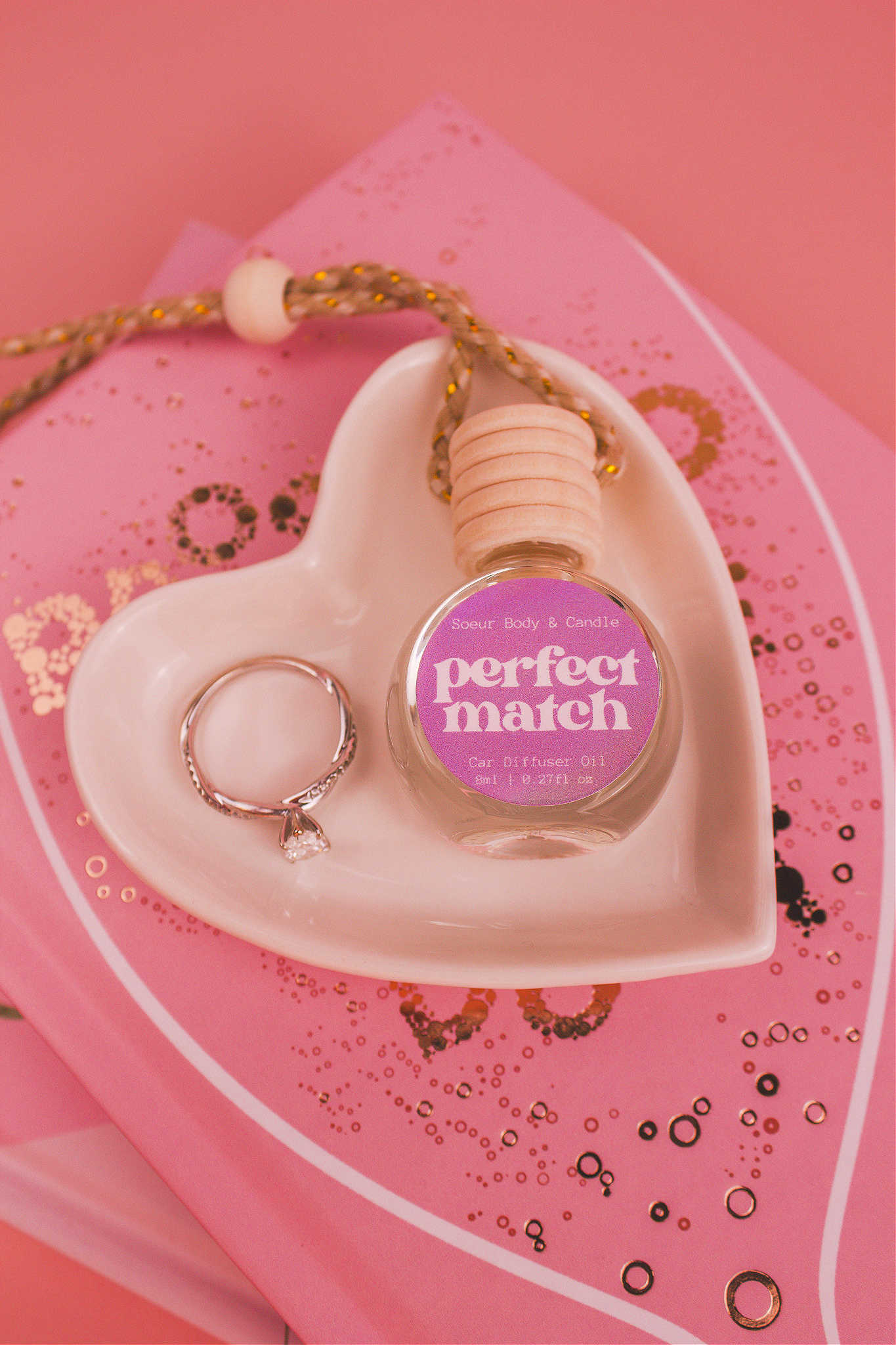 Perfect Match car diffuser in a jewelry dish with a ring beside it, sitting on top of books, with vibrant notes of cherry, almond, jasmine, rose, and vanilla.