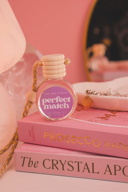 Perfect Match diffuser sitting on top of a stack of books with a jewelry dish in the background, set against a lamp, mirror, and crystals; fragrance notes: cherry, almond, jasmine, rose, and vanilla.