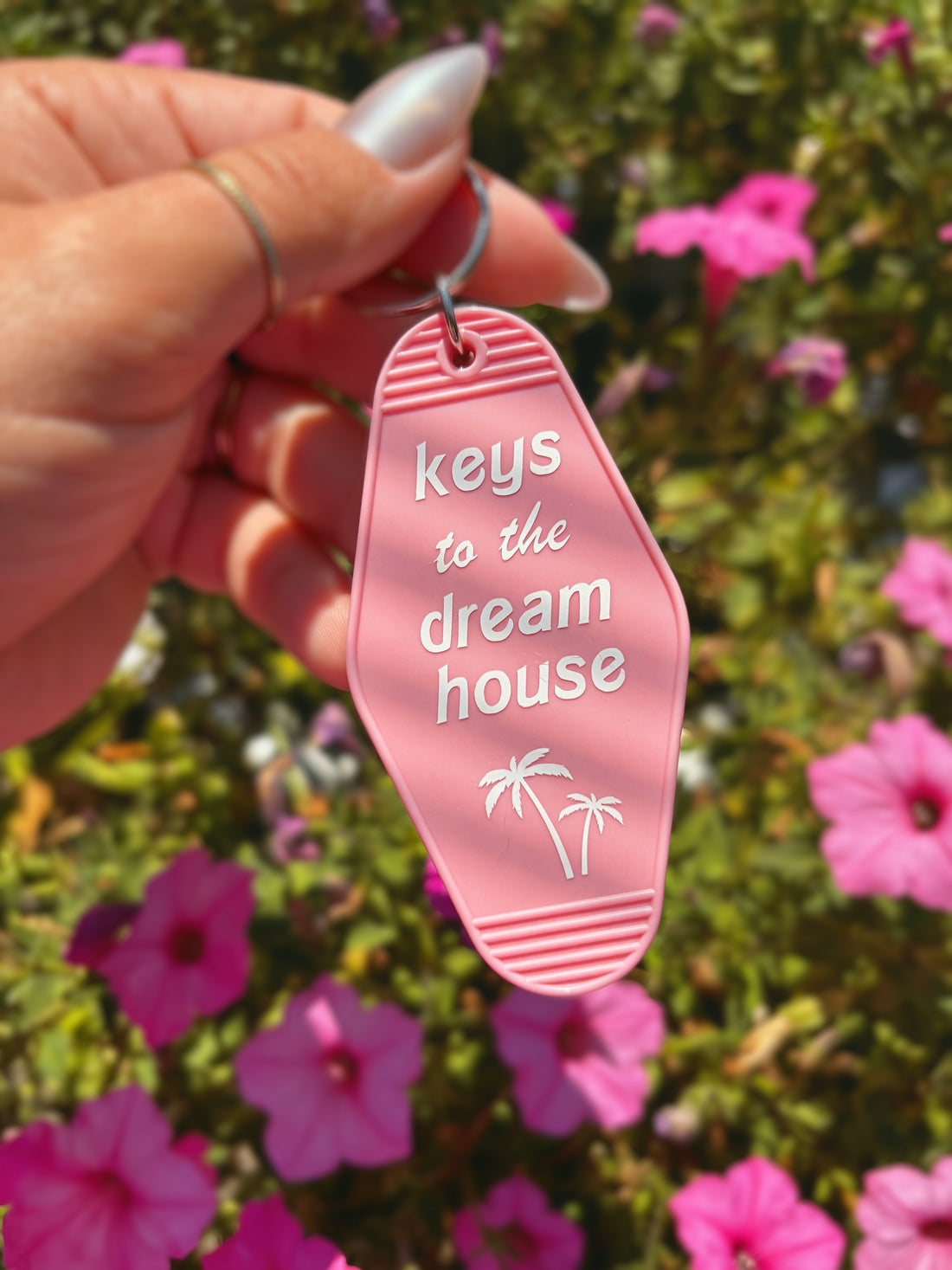 A hand holds a pink flip-flop-shaped keychain with the text &