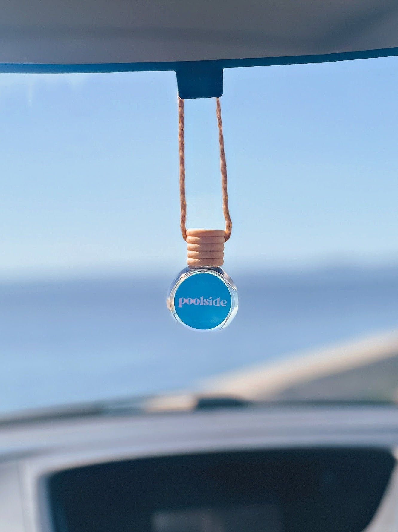 Poolside Diffuser Oil hanging from a rearview mirror, offering a balanced, long-lasting fragrance of watermelon, honeydew, strawberry, and vanilla. Perfect for cars, closets, lockers, and more.