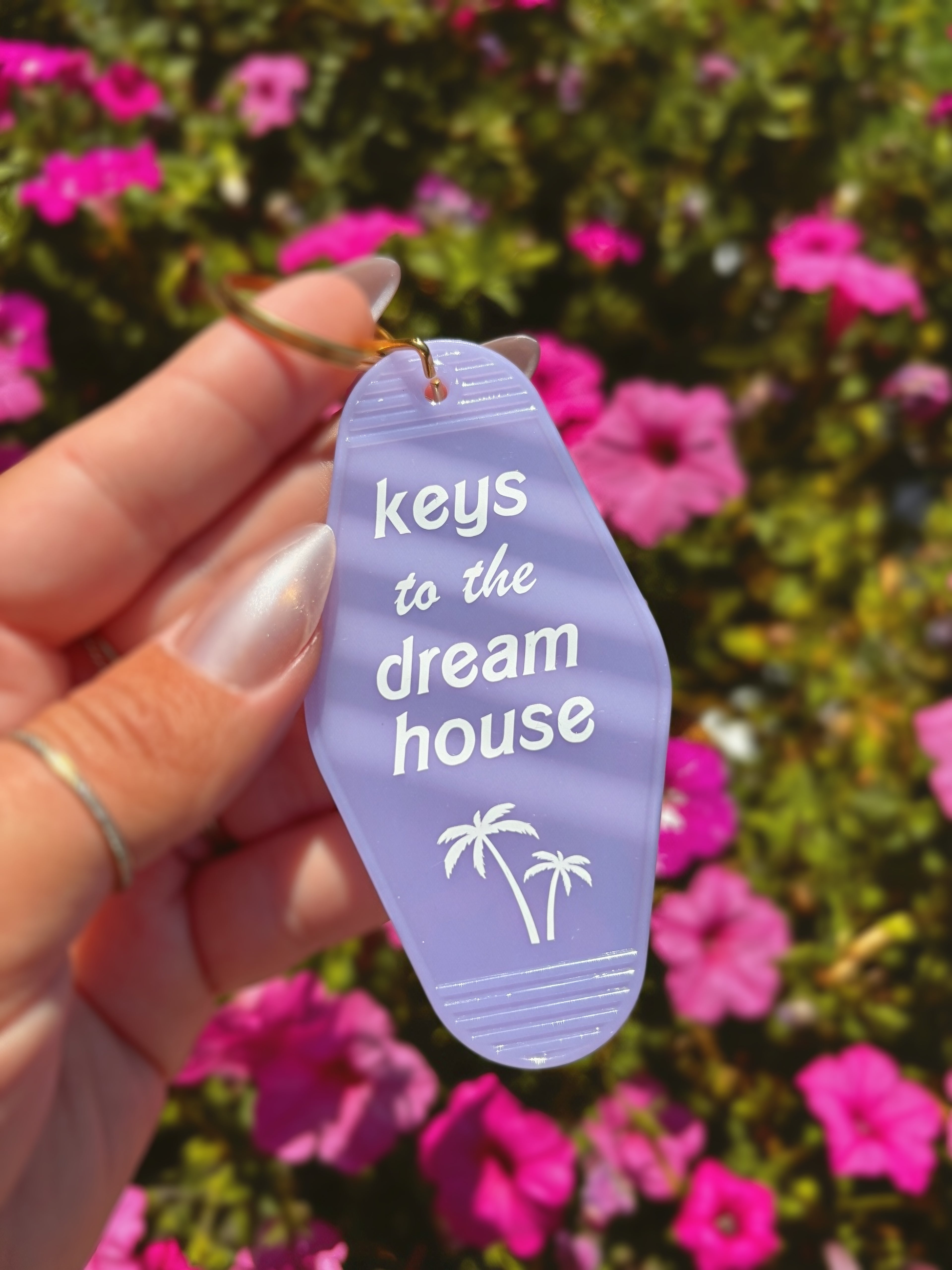 A hand holding a lavender flip-flop-shaped keychain with the text &