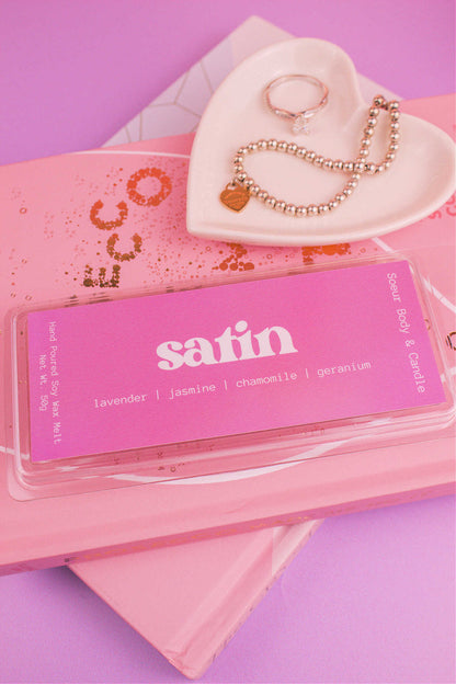 Satin wax melt displayed on books with a jewelry dish and jewelry visible in the background, showcasing its lavender, jasmine, chamomile, and geranium notes.