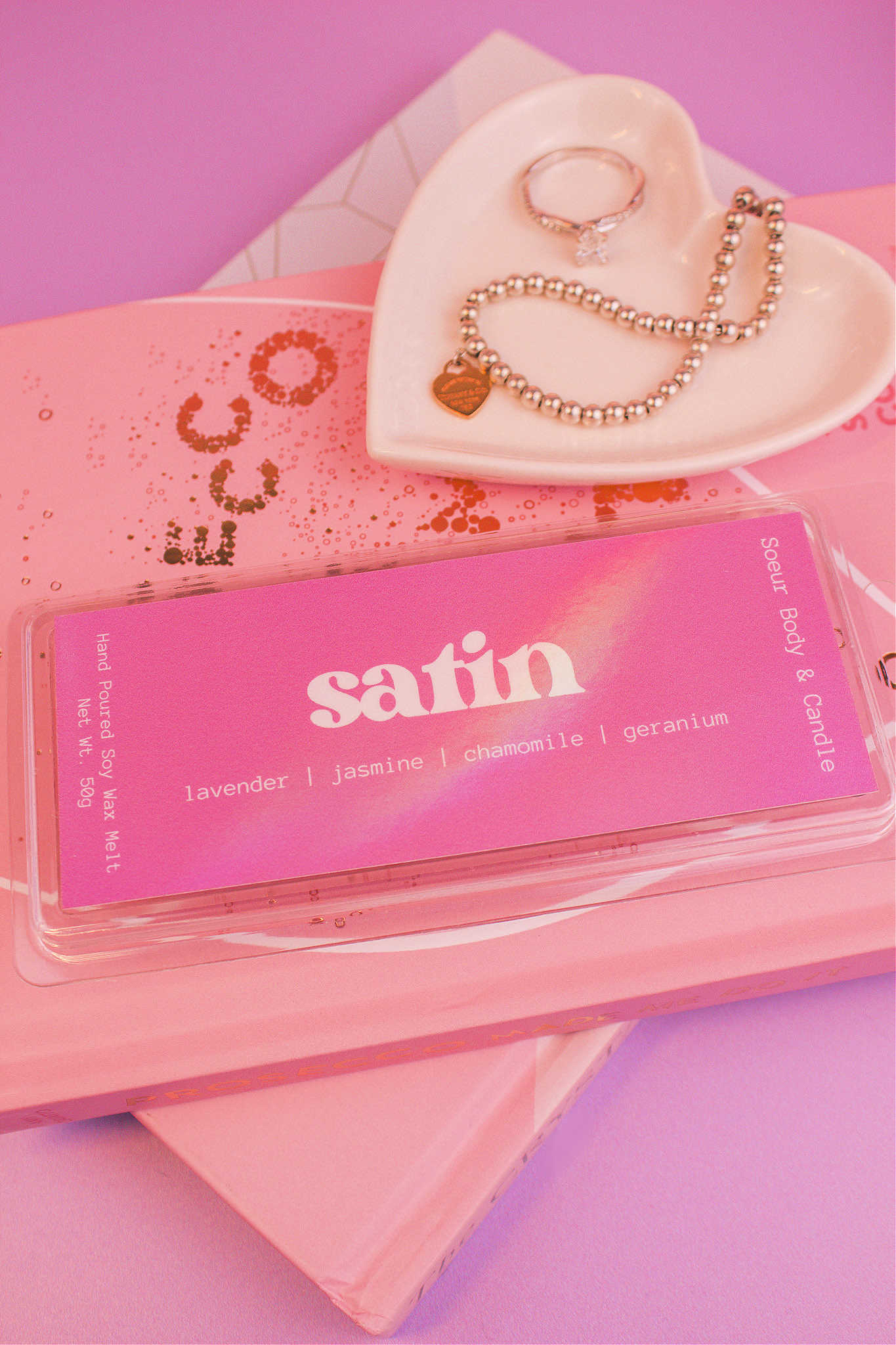 Close-up of Satin wax melt displayed on books with a jewelry dish and jewelry visible in the background, showcasing its lavender, jasmine, chamomile, and geranium notes.