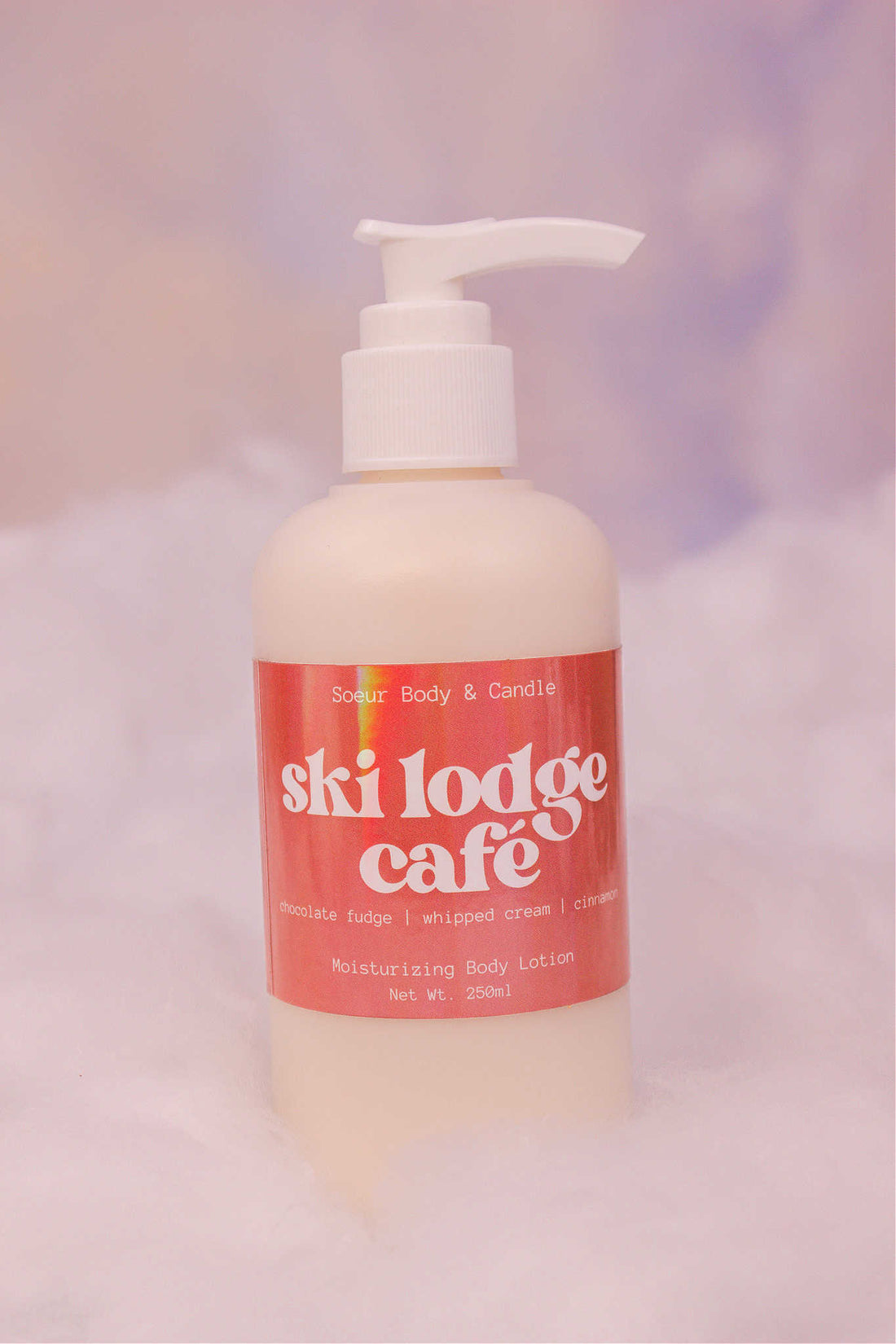 Ski Lodge Cafe body lotion sitting in fake snow against a cloudy background. Featuring notes of chocolate fudge, whipped cream, and cinnamon.