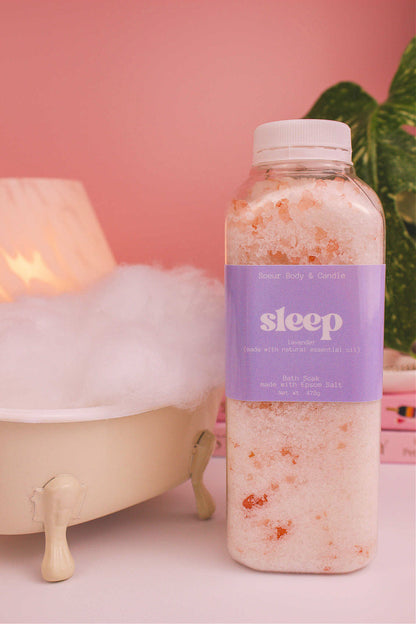 Sleep bath soak beside a small tub with bubbles, a lamp, and plants in the background, creating a relaxing vibe with lavender essential oil.