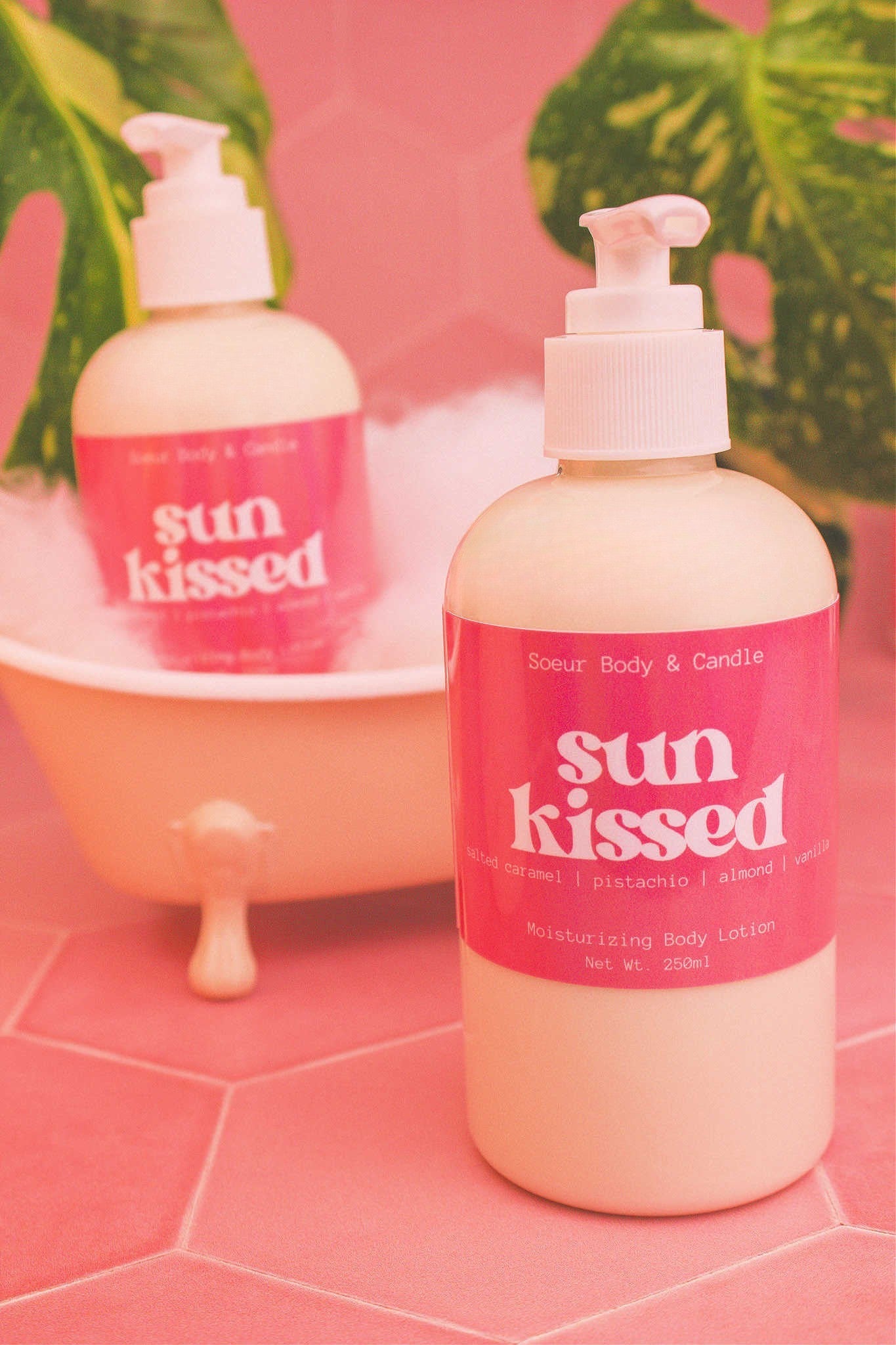 Display of two Sun Kissed body lotions in a small tub with bubbles and plants in the background, evoking a relaxing vibe with salted caramel, pistachio, almond, and vanilla notes.