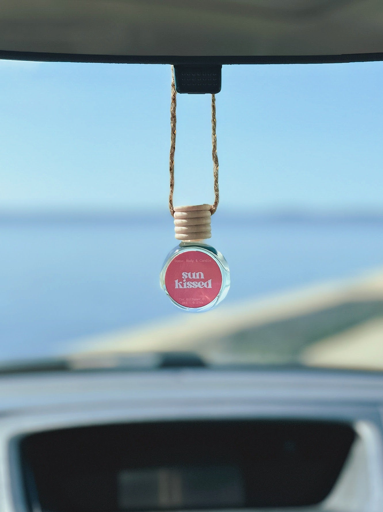 Sun Kissed Diffuser Oil hanging from a rearview mirror, offering a balanced, long-lasting fragrance of salted caramel, pistachio, almond, and vanilla. Perfect for cars, closets, lockers, and more.