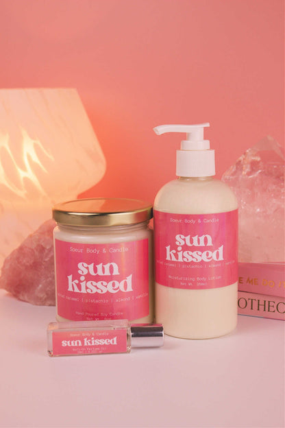 Sun Kissed body lotion presented with a matching candle and roll-on perfume, with books, a lamp, and crystals in the background; highlighting salted caramel, pistachio, almond, and vanilla notes.