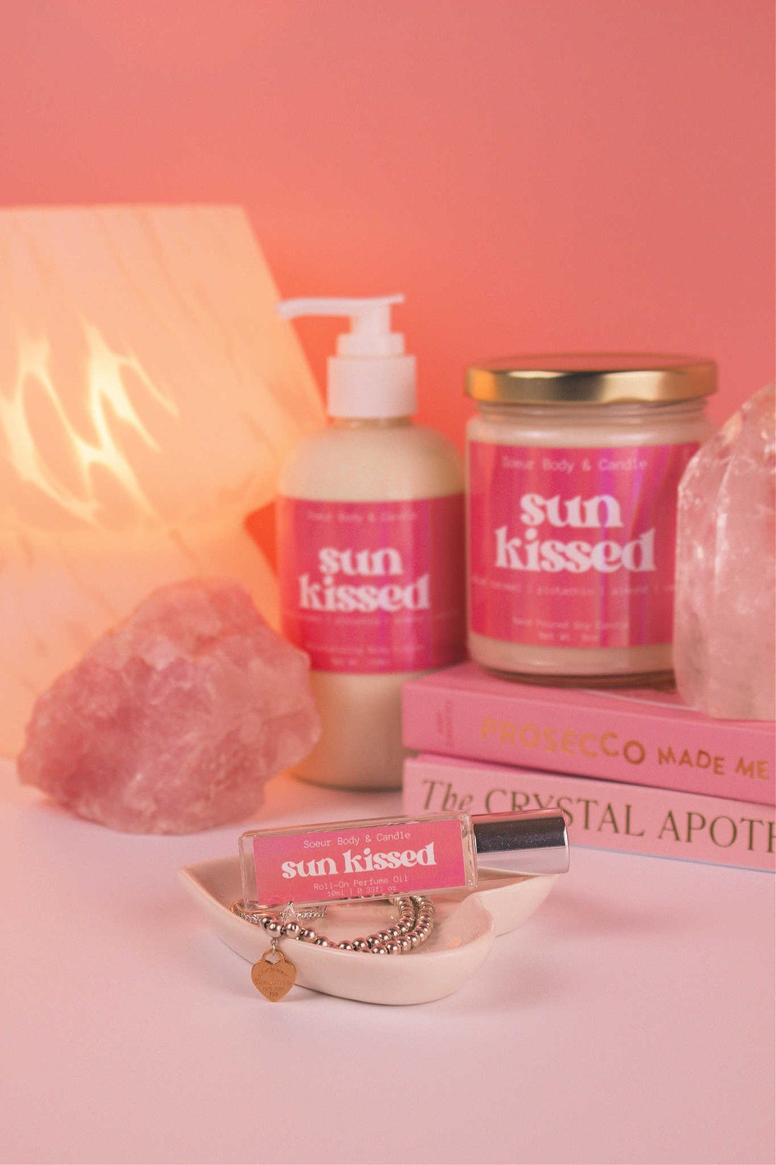 Sun Kissed roll-on perfume elegantly set in a jewelry dish with jewelry, and coordinating lotion and candle, along with books, a lamp, and crystals in the background. Featuring notes of salted caramel, pistachio, almond, and vanilla.