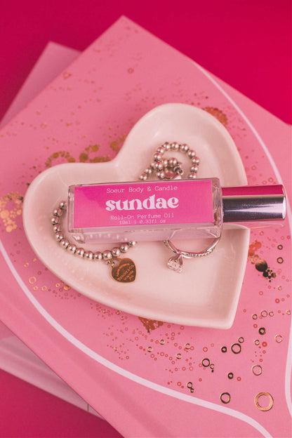 Sundae roll-on perfume bottle displayed in a jewelry dish beside a ring and bracelet, featuring notes of sweet cream, vanilla, and sugary waffle cone.