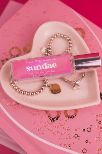 Close-up of Sundae roll-on perfume bottle displayed in a jewelry dish beside a ring and bracelet, featuring notes of sweet cream, vanilla, and sugary waffle cone.