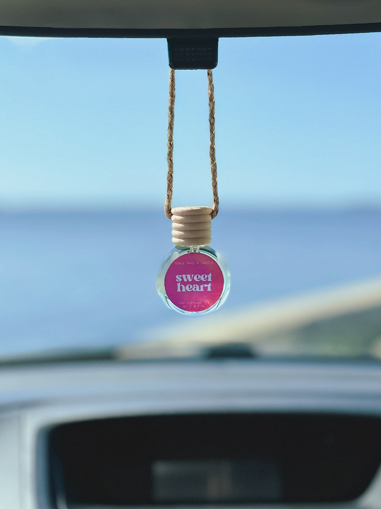 Sweet Heart Diffuser Oil hanging from a rearview mirror, offering a balanced, long-lasting fragrance of plum, raspberry, violet, sugar, and vanilla. Perfect for cars, closets, lockers, and more.