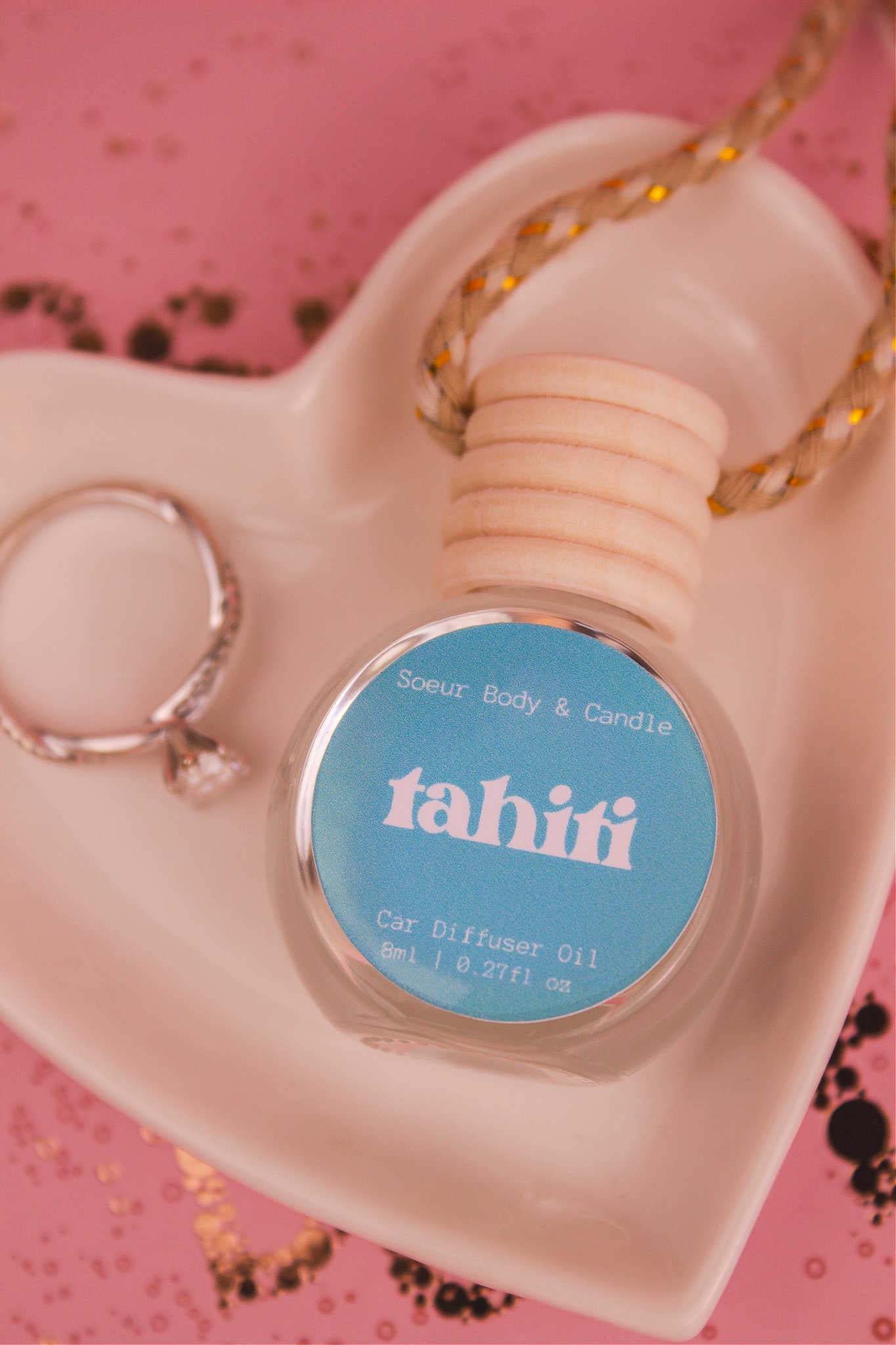 Close-up of Tahiti car diffuser in a jewelry dish with a ring beside it, featuring a sweet blend of sugar, vanilla, almond, amber, and oak moss notes.