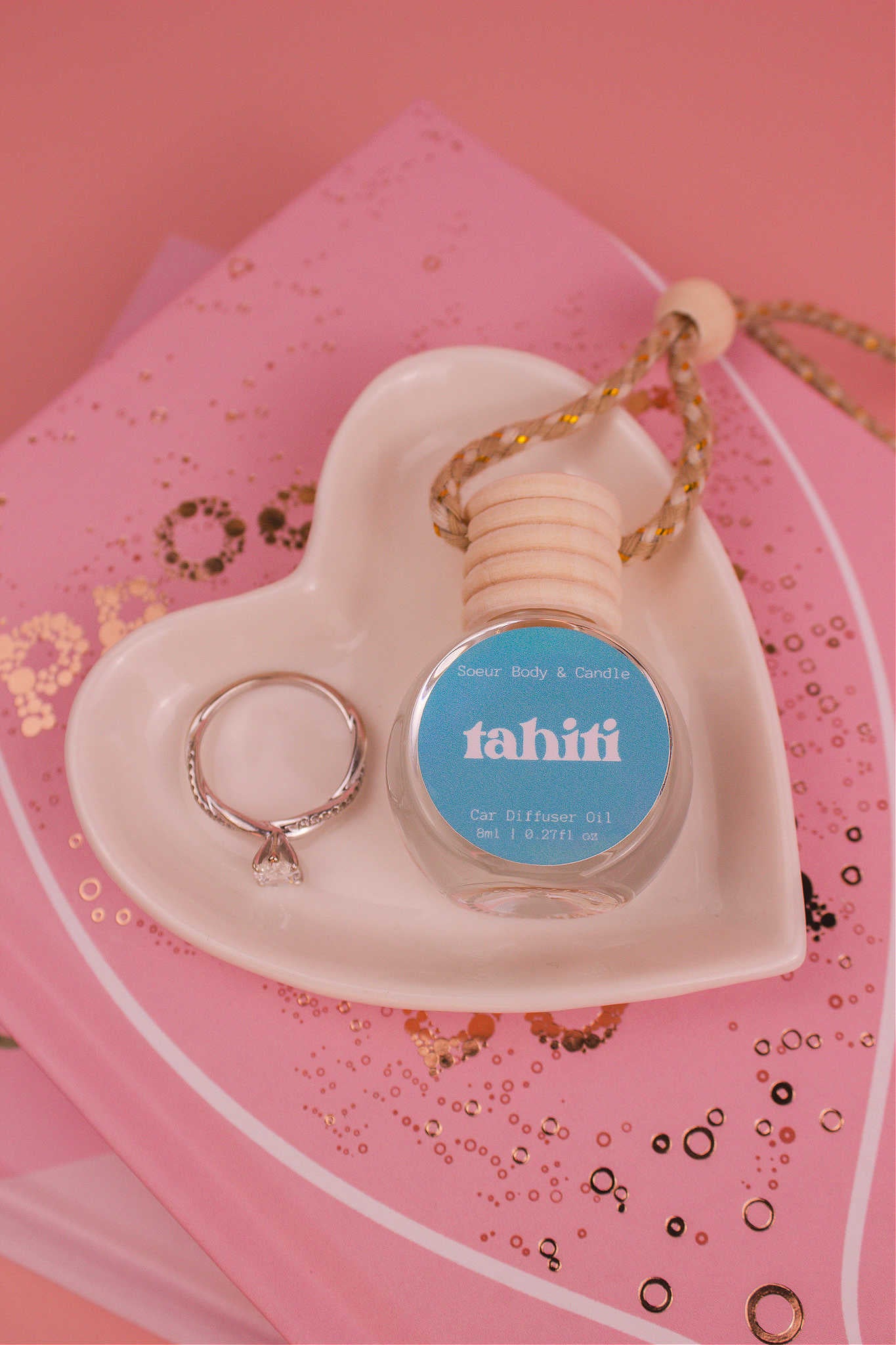 Tahiti car diffuser in a jewelry dish with a ring beside it, sitting on top of books, featuring a sweet blend of sugar, vanilla, almond, amber, and oak moss notes.