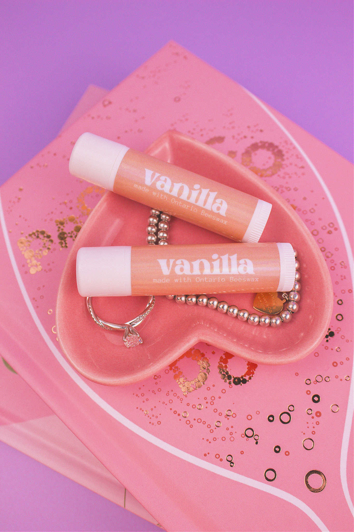 Two Vanilla flavoured lip balms displayed in a jewelry dish with a ring and bracelet, sitting on top of books.