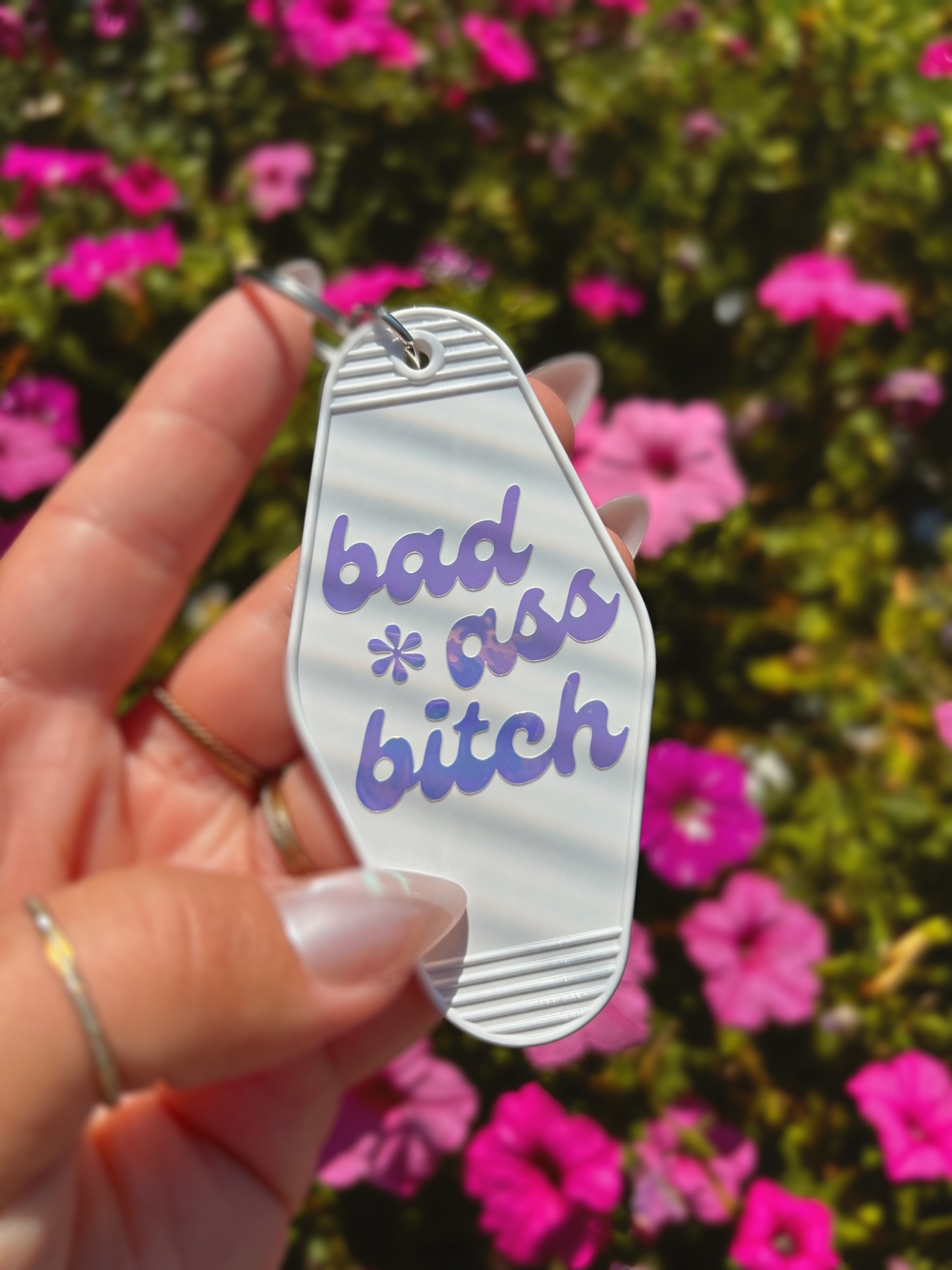 A hand holding a white motel-style keychain with holographic text reading &