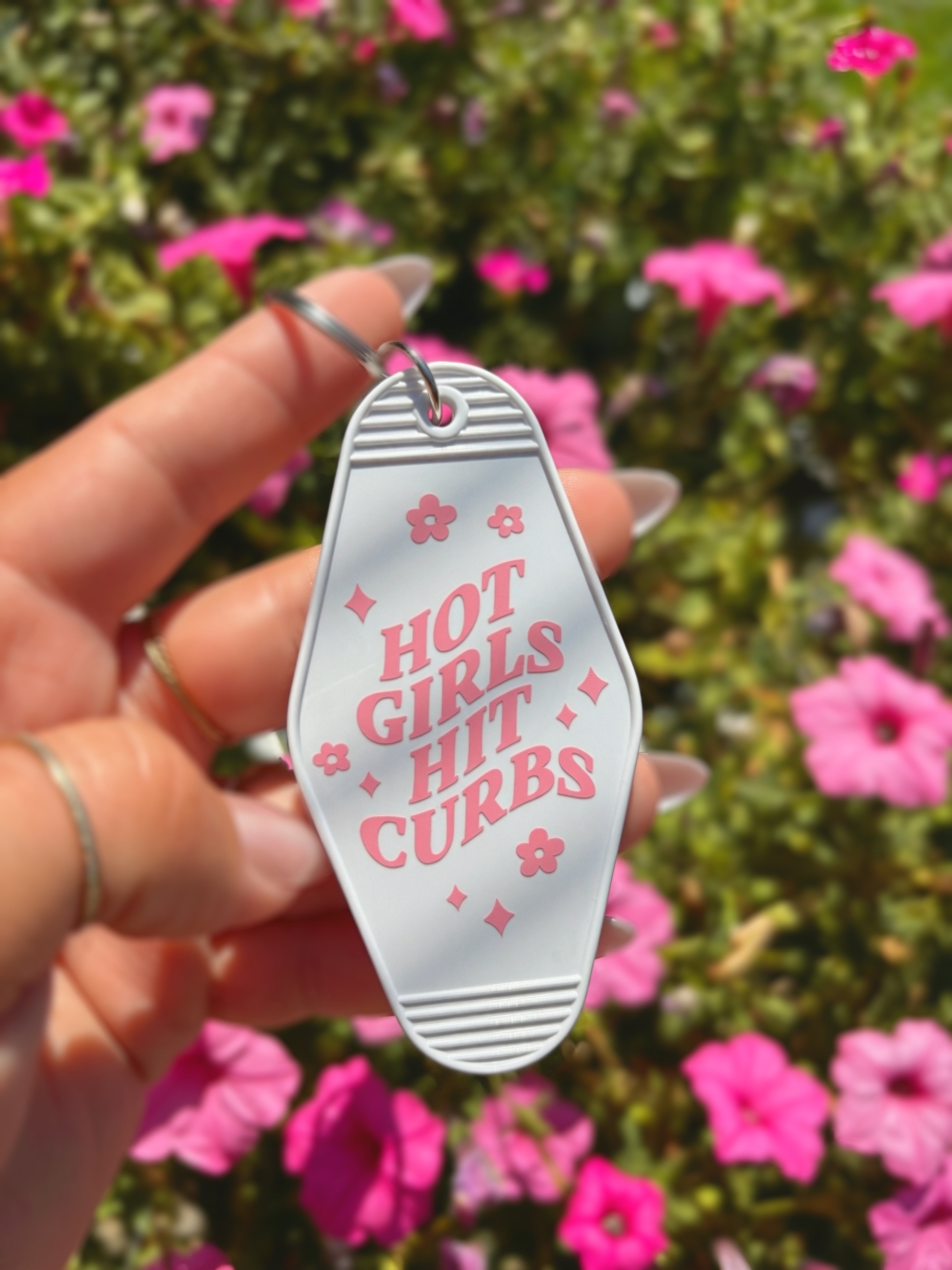 A hand holding a white motel-style keychain with pink text reading &